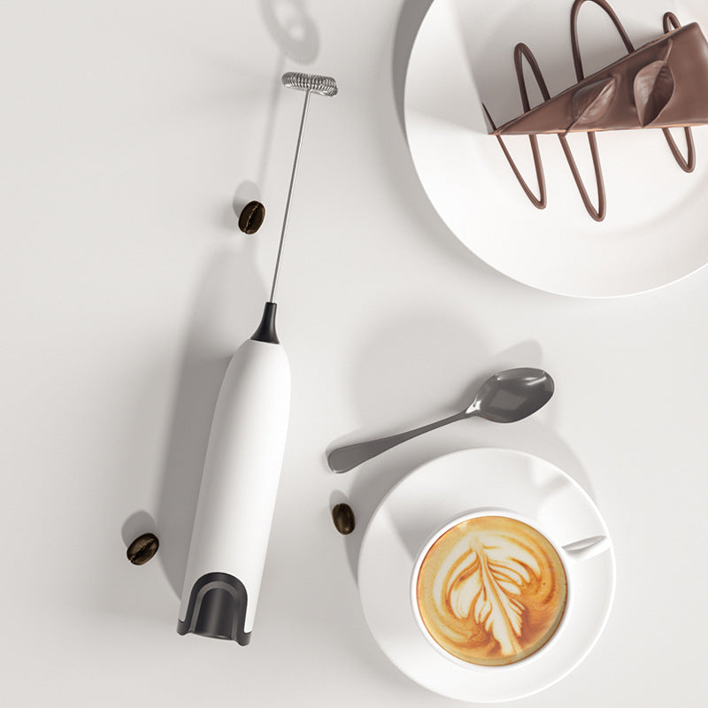 Bombom mini handheld milk frother in white next to a cup of latte with latte art and coffee beans