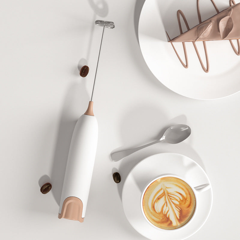 Bombom mini handheld milk frother in white and tan next to a cup of latte with leaf latte art